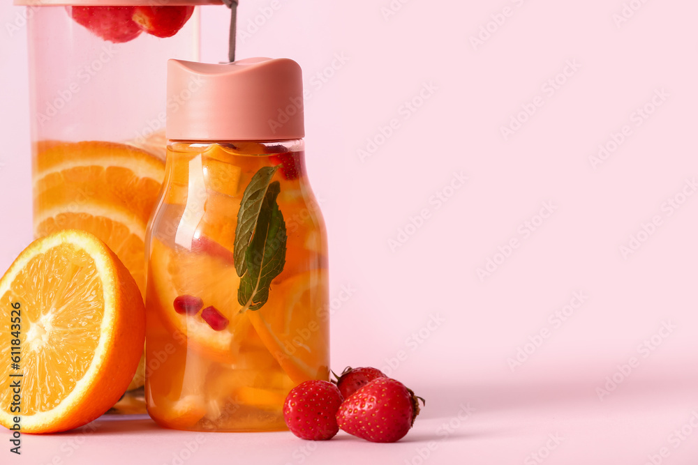 Sports bottles of infused water with different sliced fruits on pink background