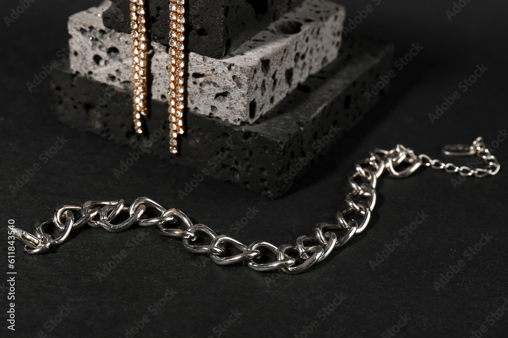 Decorative podium with beautiful chain bracelet and earrings on black background