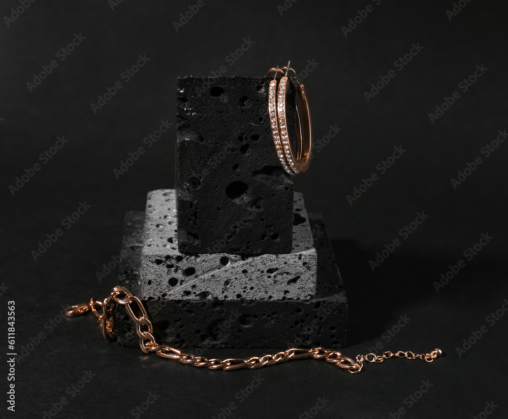 Decorative podium with beautiful chain bracelet and earrings on black background