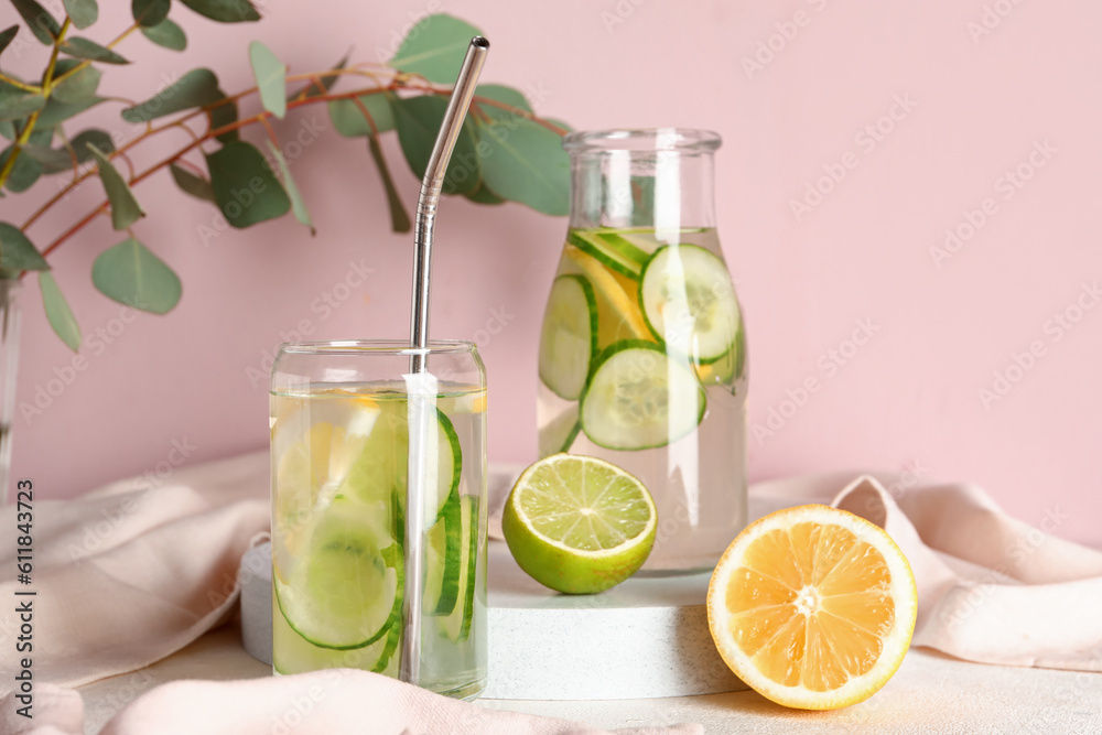 Glass and bottle of infused water with cucumber slices on pink background