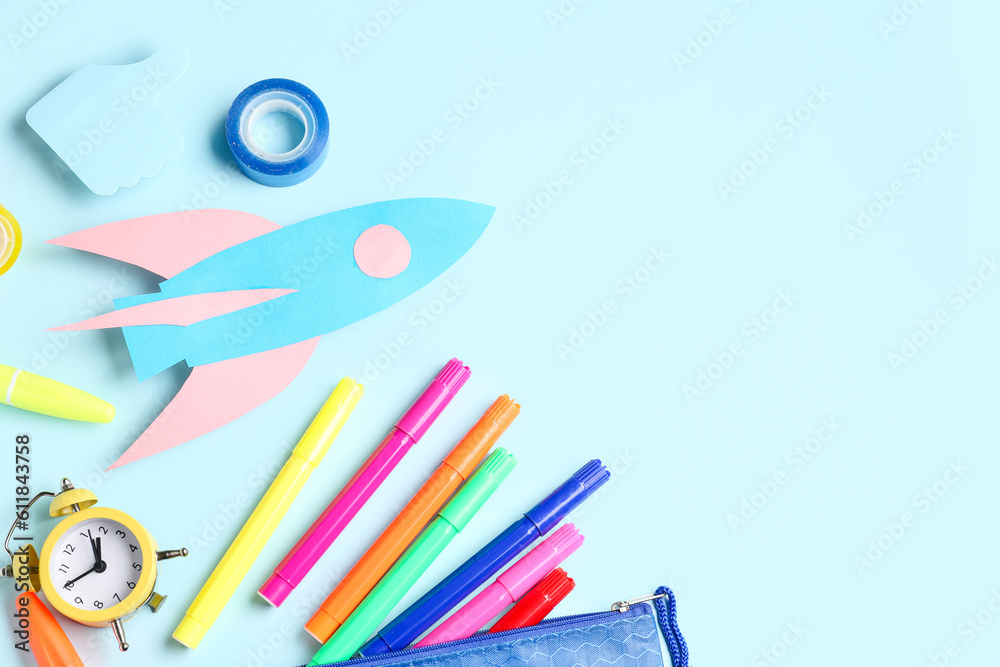 Paper rocket with pencil case and different stationery on blue background