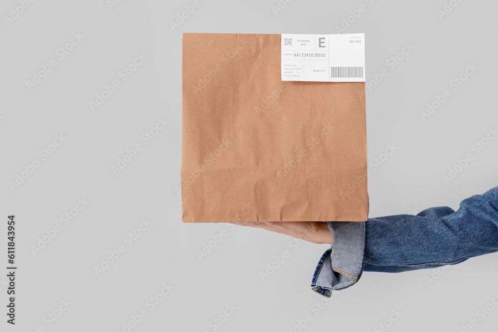 Female hand holding paper bag on grey background. Food delivery