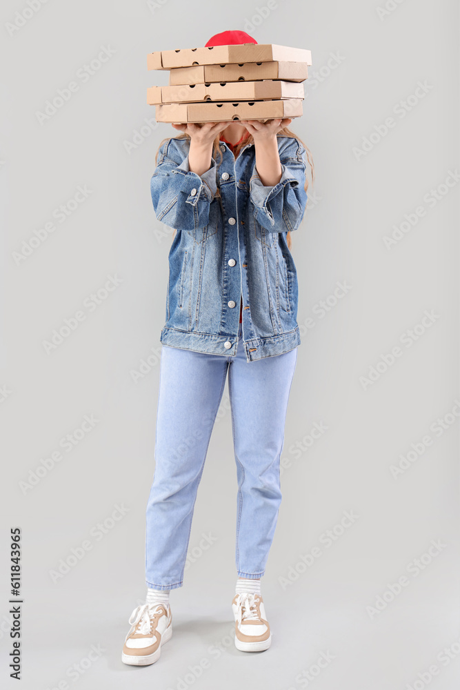 Female courier holding many pizza boxes on grey background