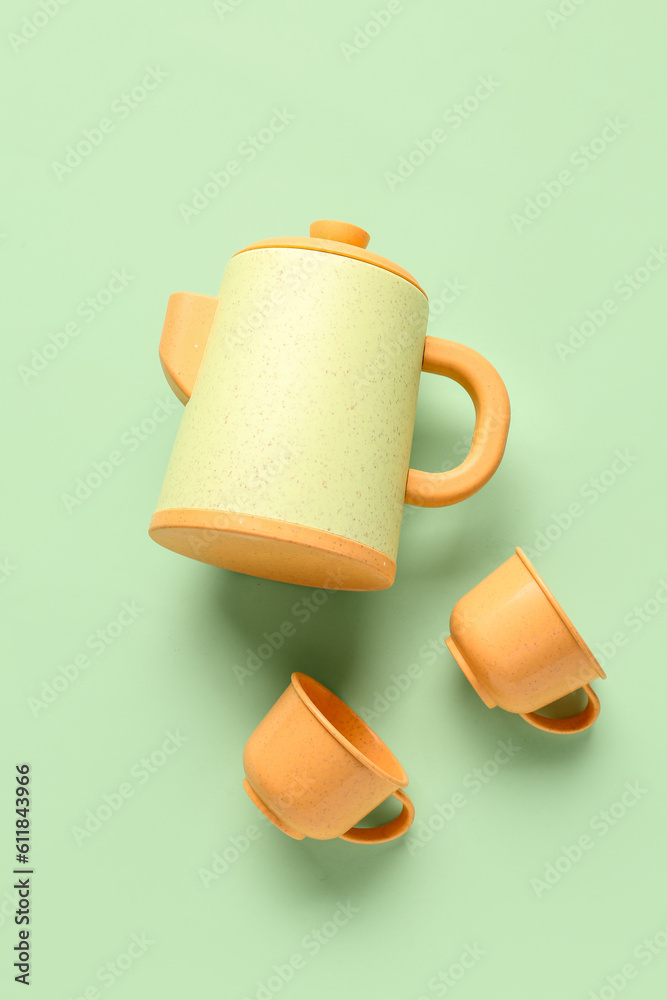 Teapot with cups for baby on pale green background