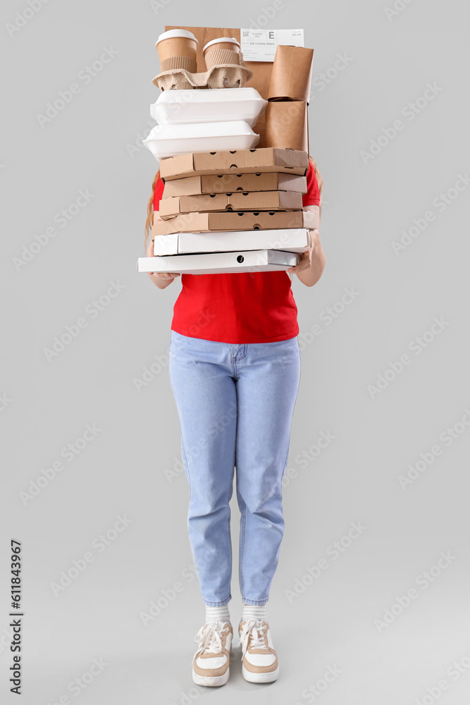 Female courier holding many boxes and containers with food on grey background