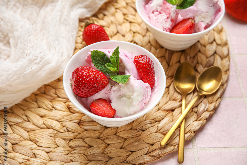 Bowls of strawberry ice cream and spoons on wicker mat, closeup