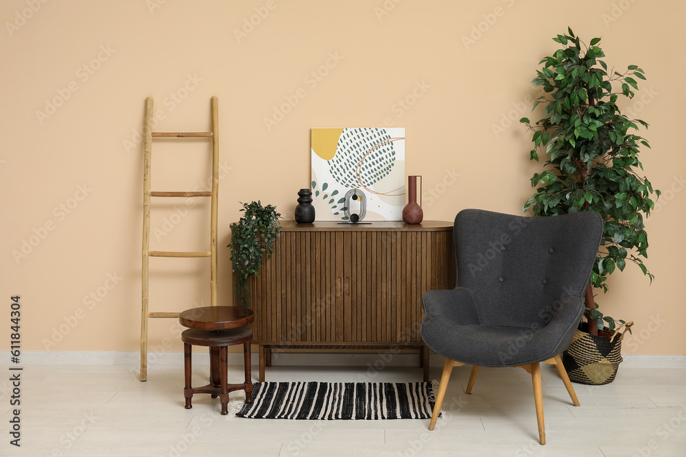 Dark grey armchair with dresser, houseplants and ladder near beige wall