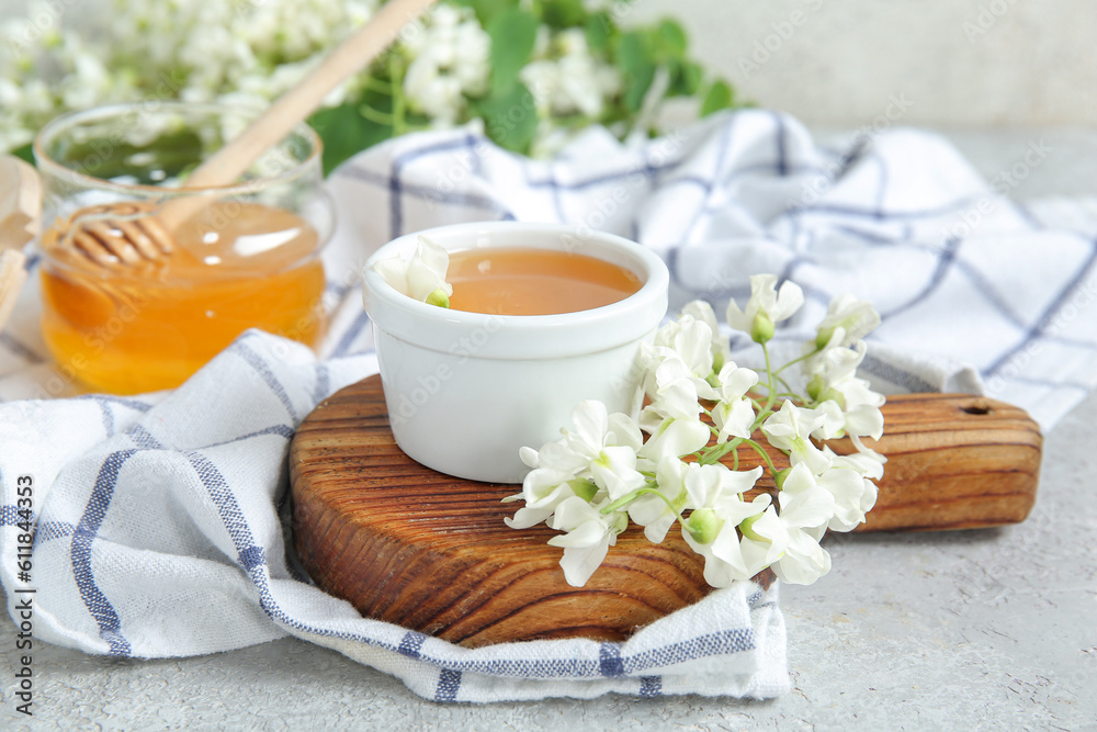 Bowl of honey with flowers of acacia on light background, closeup