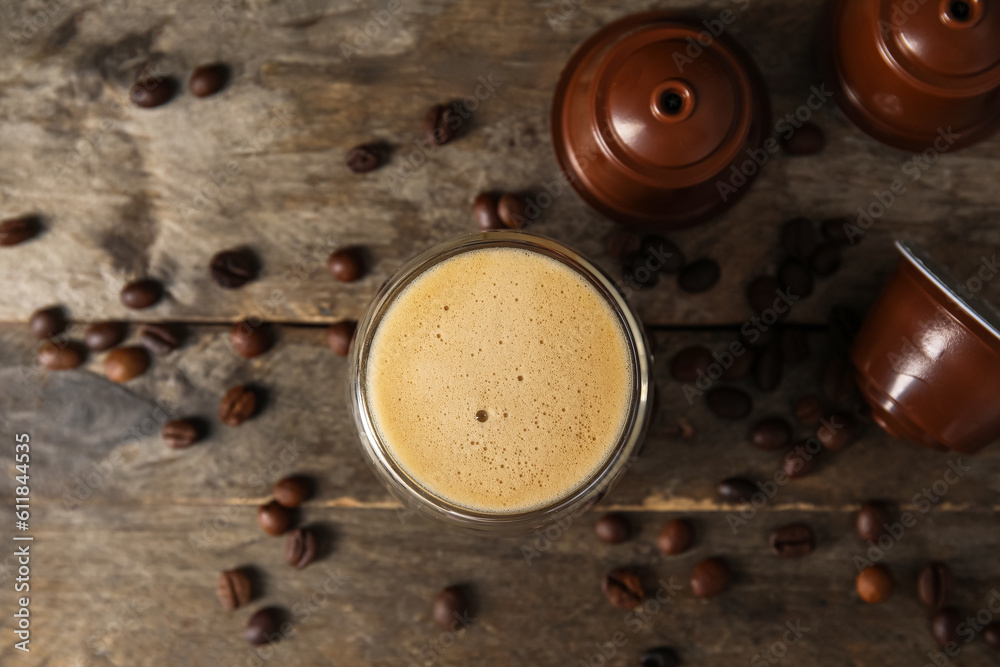 Cup of delicious coffee, capsules and beans on wooden table