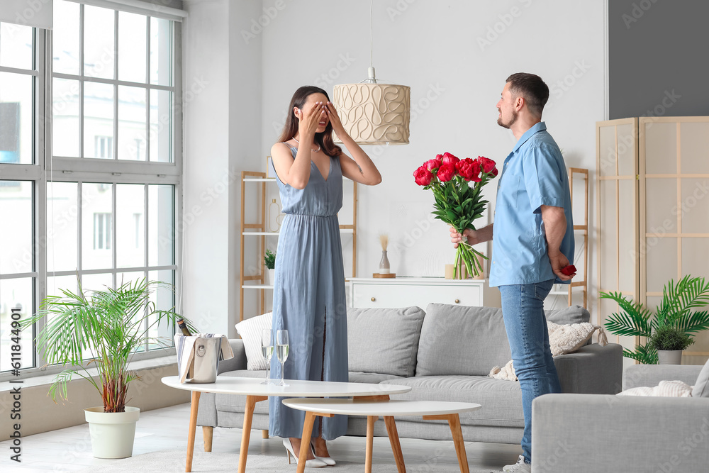 Young man with flowers proposing to his girlfriend at home