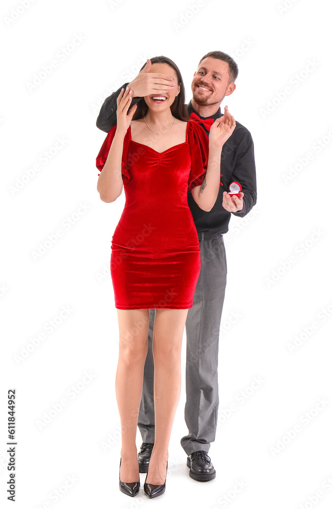 Young man with engagement ring closing his girlfriends eyes on white background