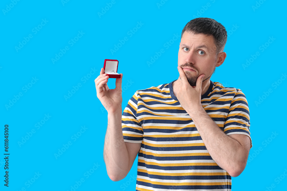 Thoughtful young man with engagement ring on blue background