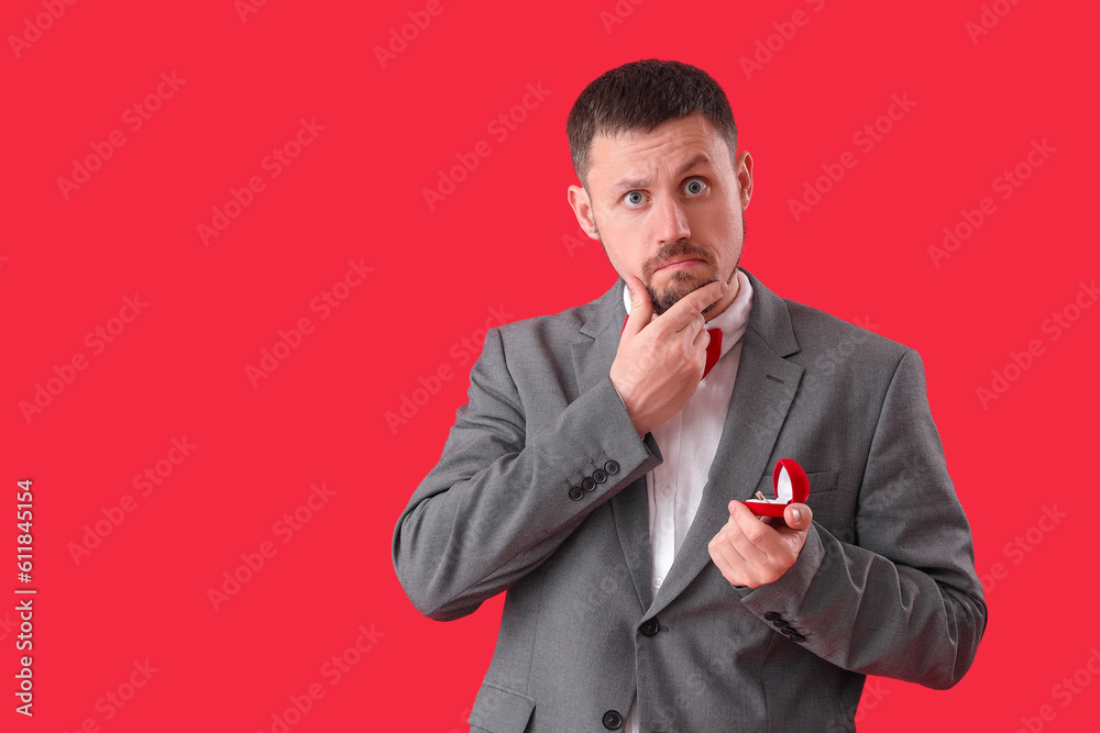 Handsome man with engagement ring on red background