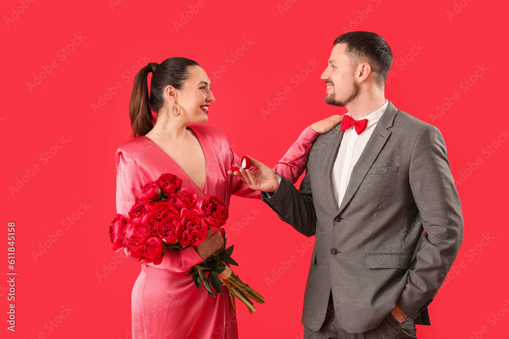 Young man proposing to his girlfriend with flowers on red background