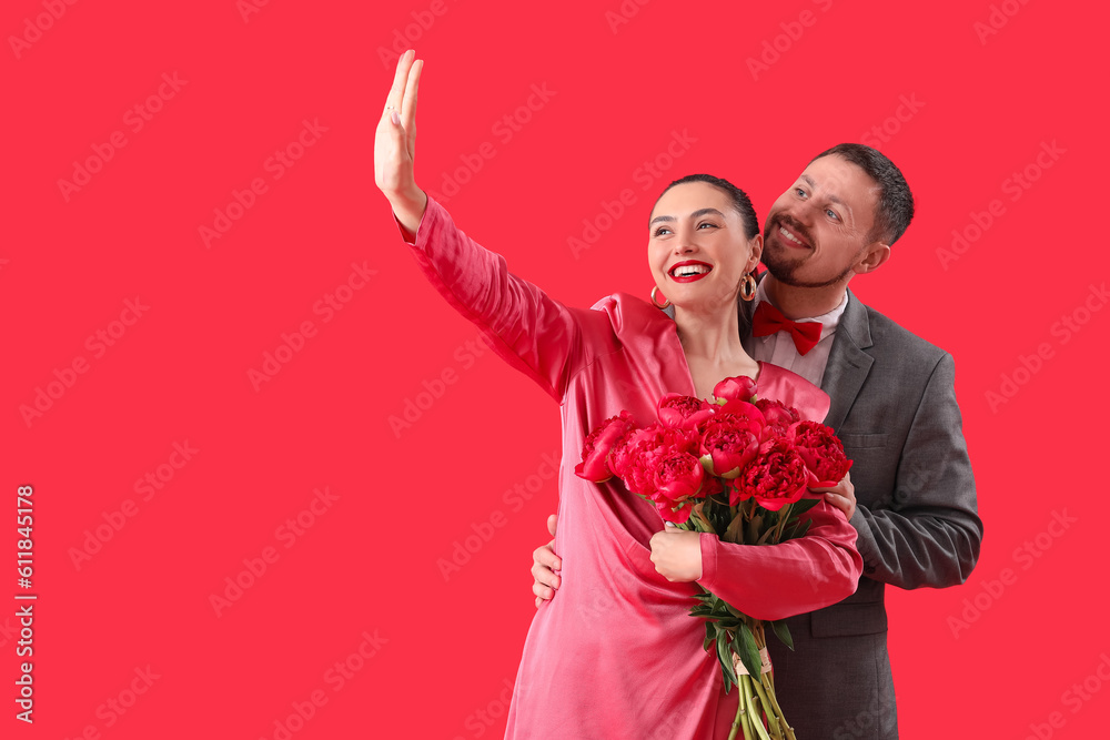 Happy engaged couple with flowers taking selfie on red background