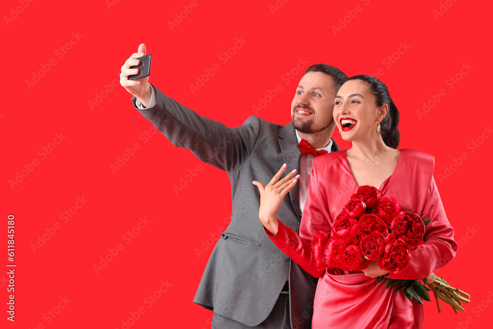 Happy engaged couple with flowers taking selfie on red background