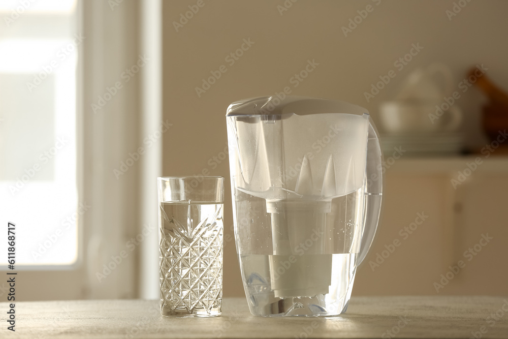 Water filter jug and glass on table in kitchen