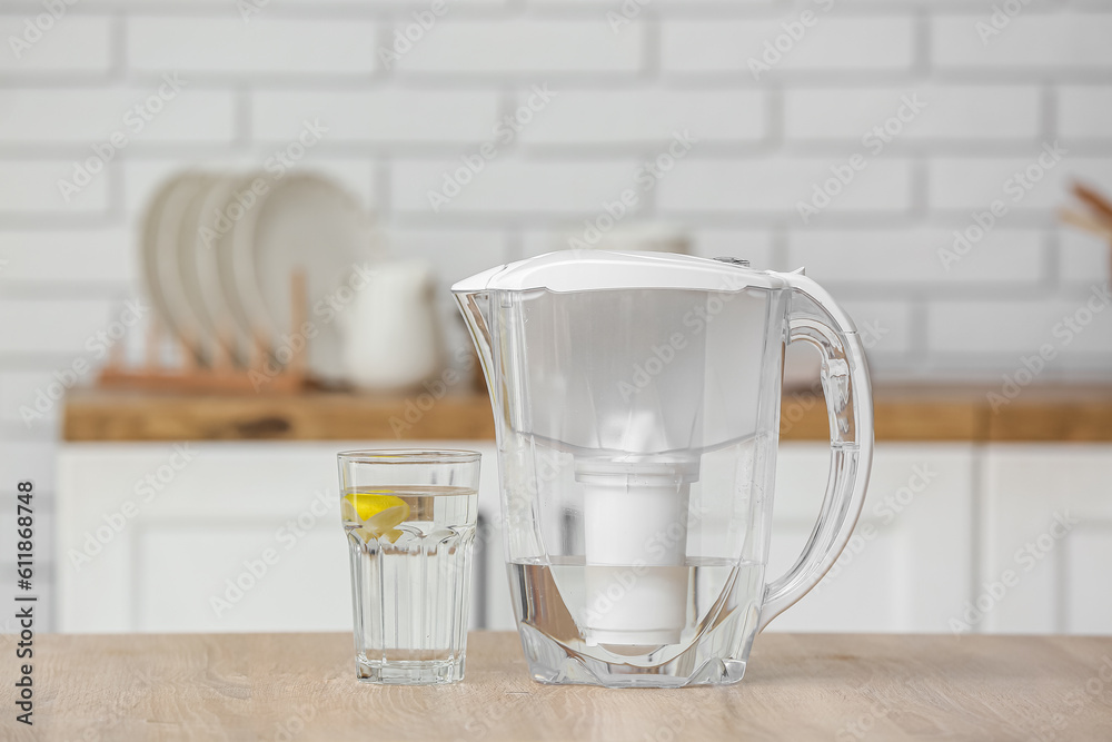 Water filter jug with glass on table in modern kitchen