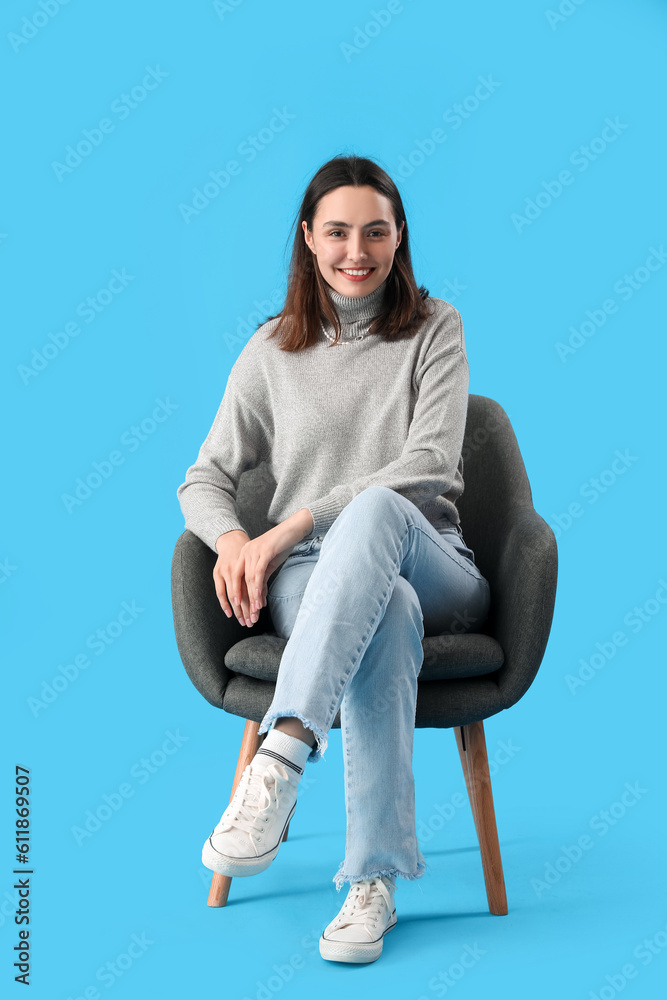 Young woman sitting in black armchair on blue background