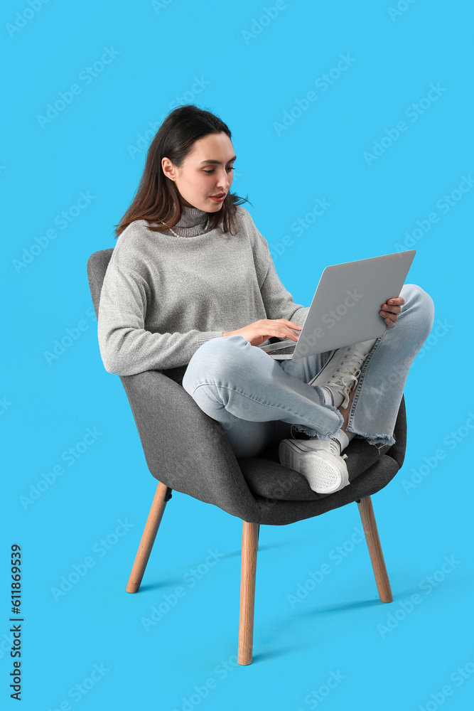 Young woman using laptop in black armchair on blue background