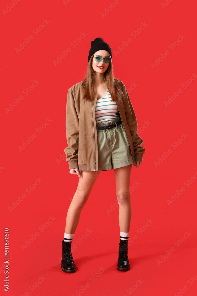 Stylish young woman in sunglasses on red background