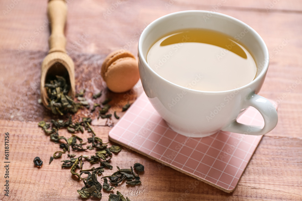 Drink coaster with cup of tea, macaroon and scattered leaves on wooden table, closeup