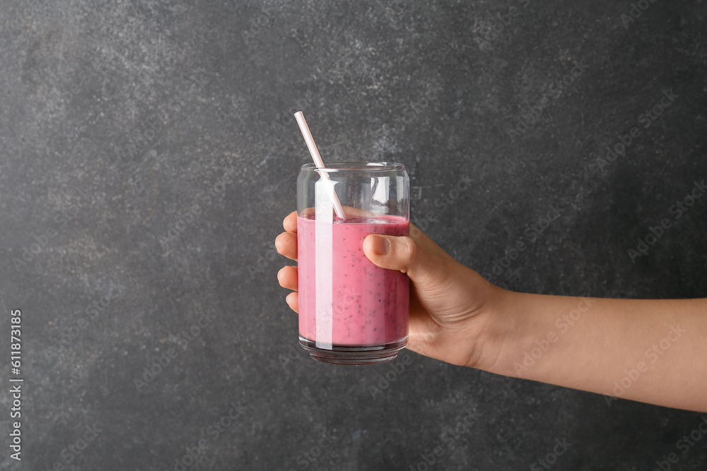 Female hand with glass of pink smoothie on dark background