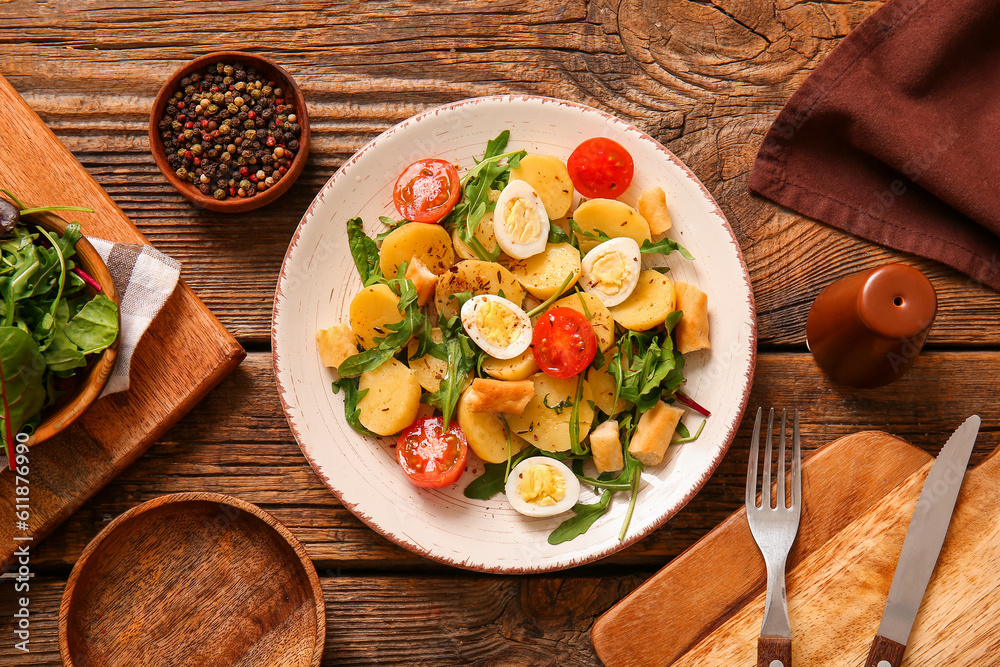 Plate of tasty potato salad with eggs and tomatoes on wooden background, top view