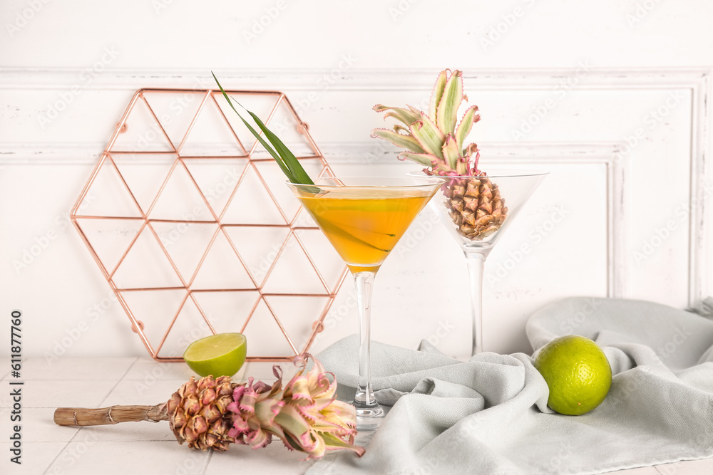 Glass of cocktail with baby pineapples and lime on table near light wall