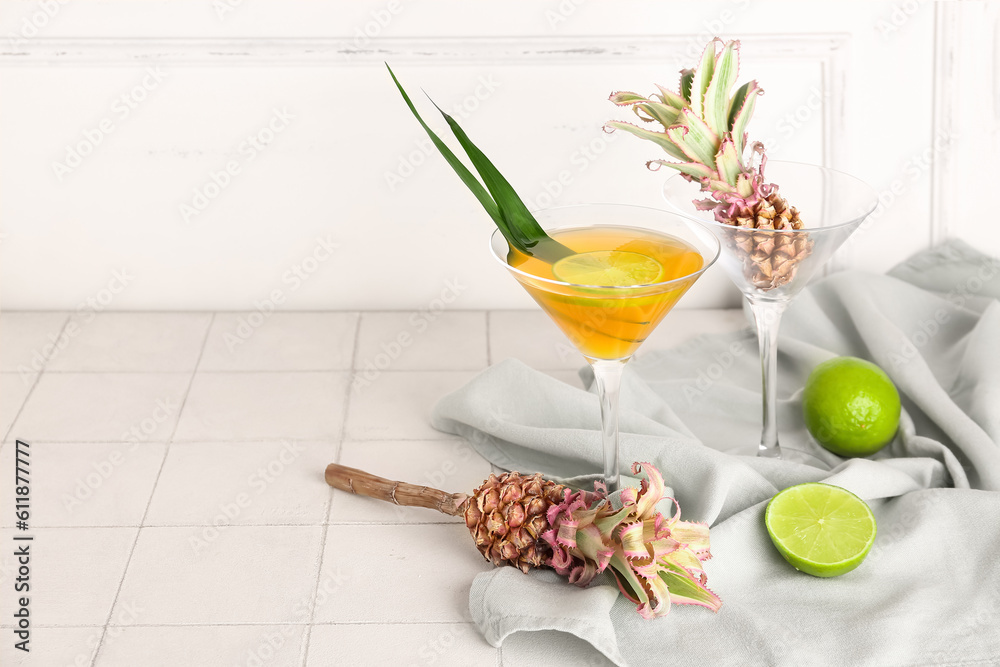 Glass of cocktail with baby pineapples and lime on table near light wall