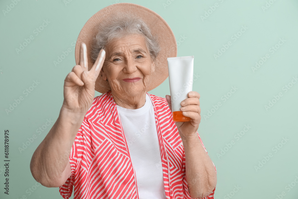 Senior woman with sunscreen cream showing victory gesture on green background