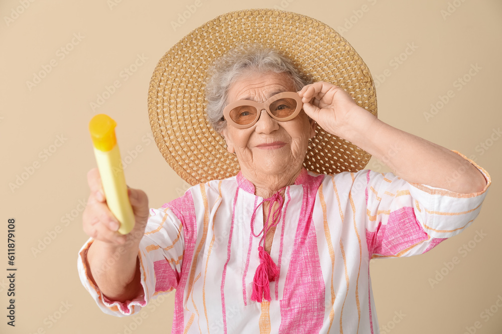 Senior woman with sunscreen cream on beige background