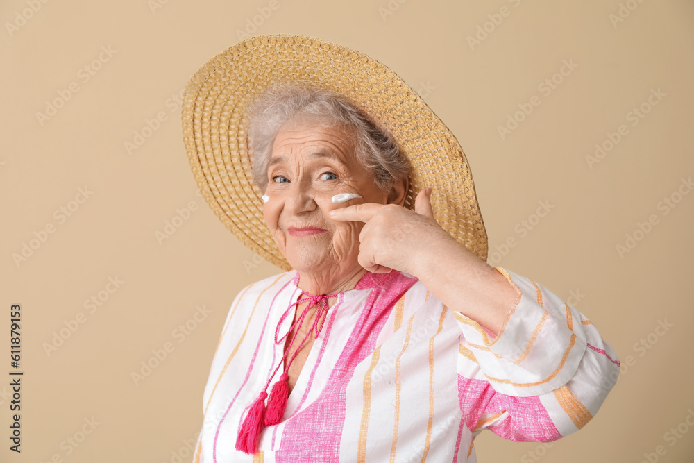 Senior woman with sunscreen cream on her face against beige background