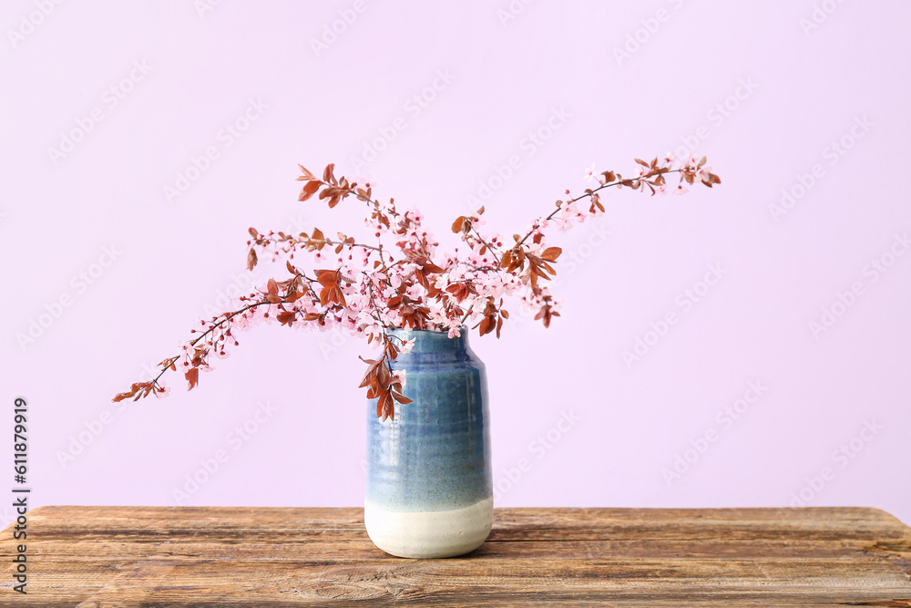 Vase with blooming tree branches on wooden table against pink background