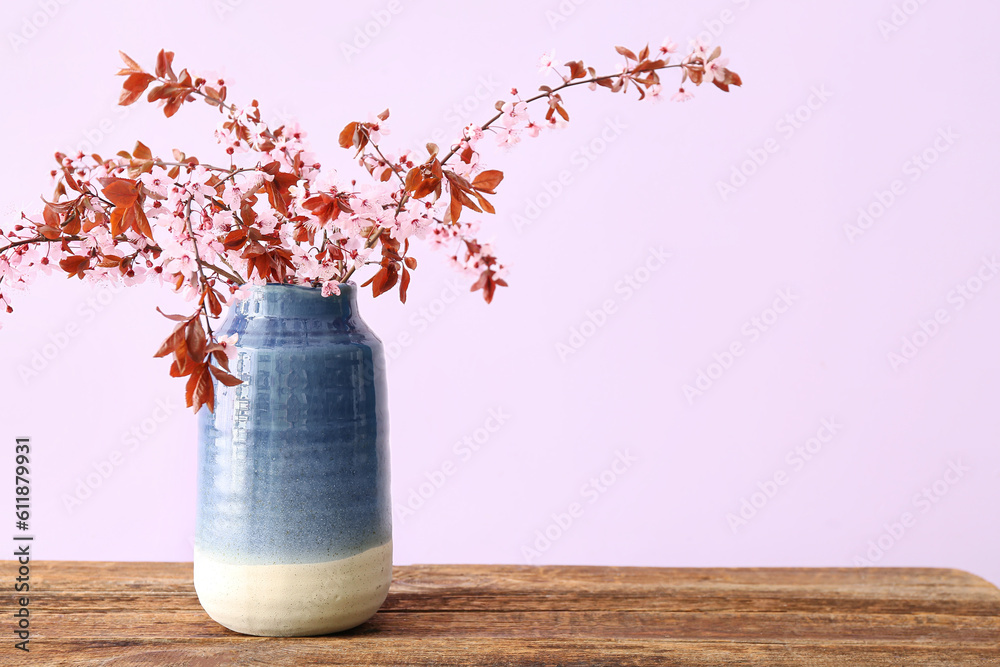 Vase with blooming tree branches on wooden table against pink background