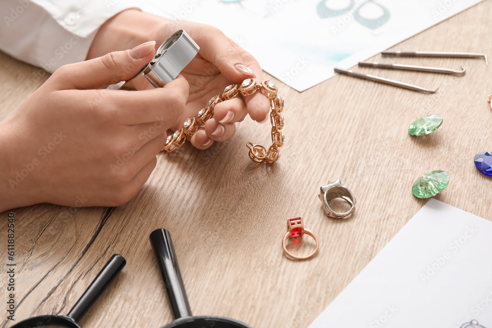 Female jeweler examining bracelet on wooden table, closeup