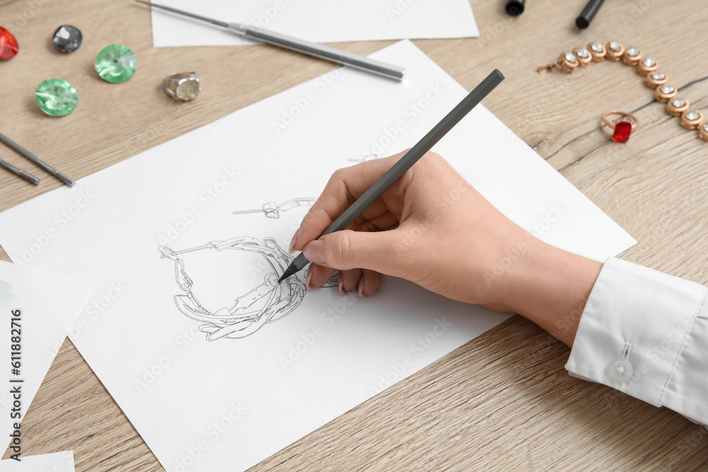 Female jeweler drawing adornment on wooden table, closeup