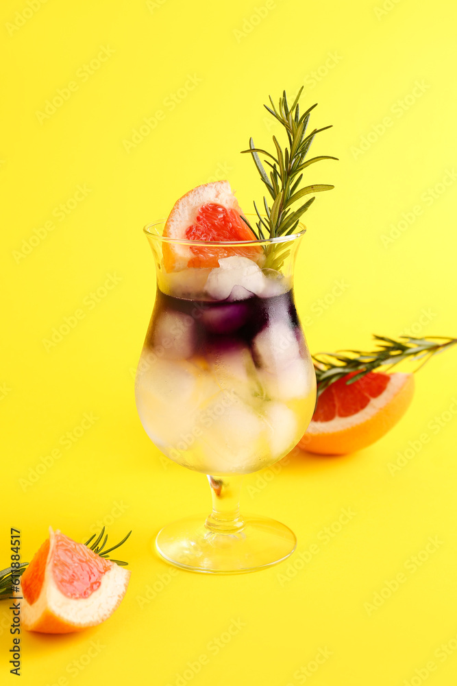 Glass of purple gin and tonic with grapefruit and rosemary on yellow background