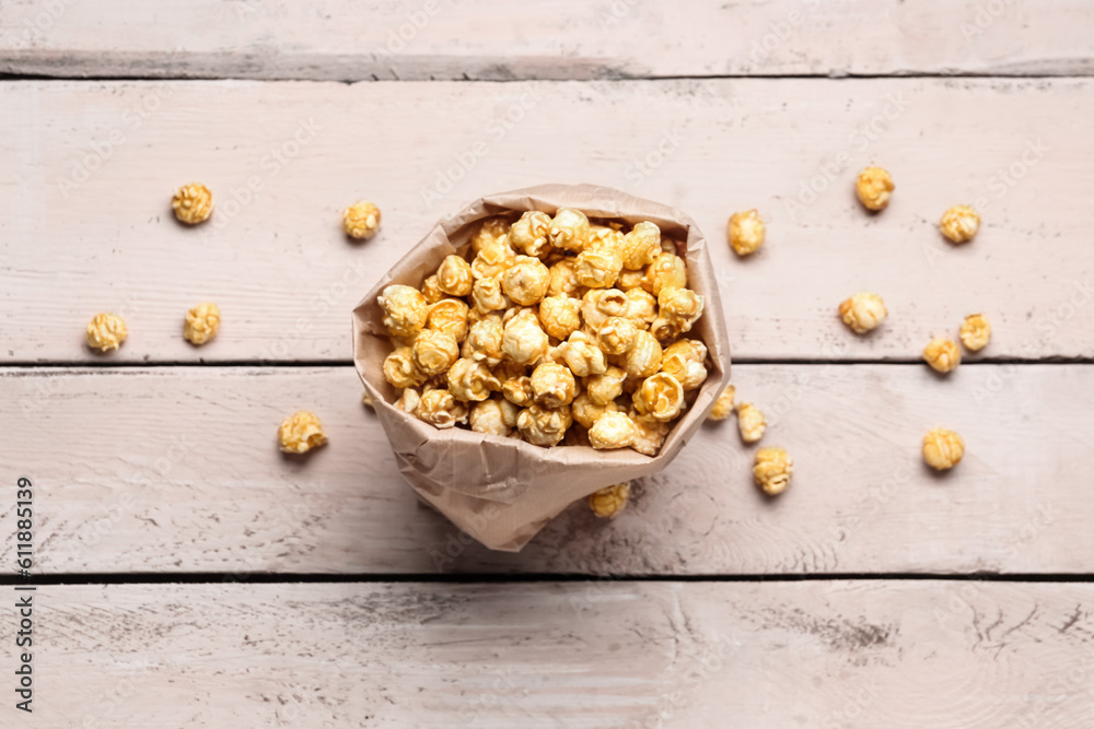 Paper bag with crispy popcorn on white wooden background