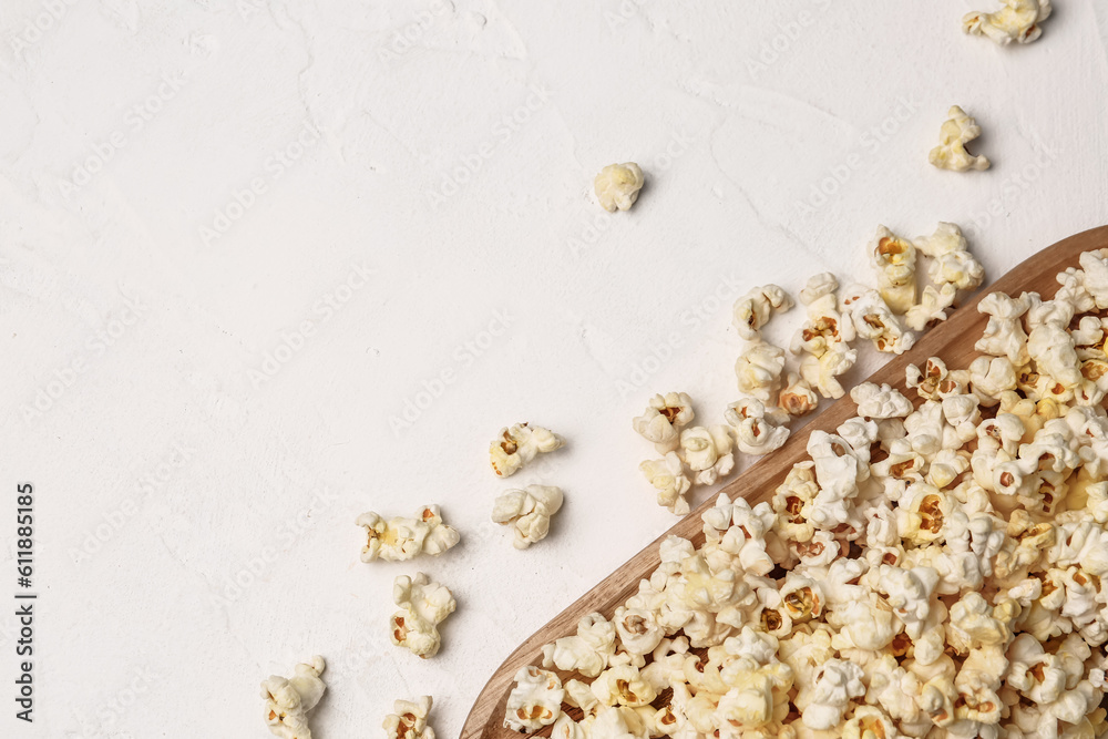 Wooden board with crispy popcorn on light background