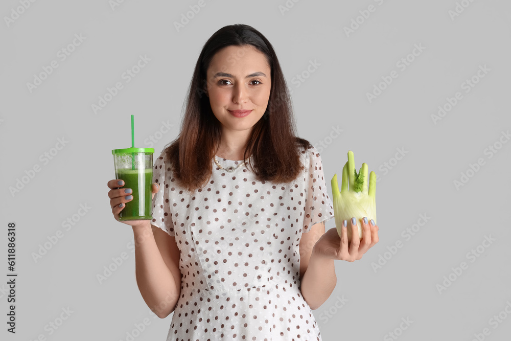 Young woman with glass of vegetable juice and celery on grey background