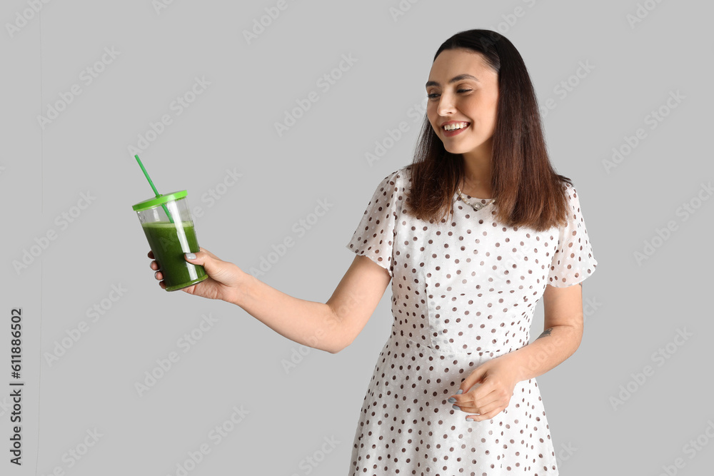 Young woman with glass of vegetable juice on grey background