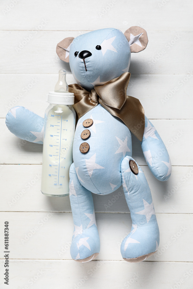 Teddy bear with bottle of milk for baby on white wooden background