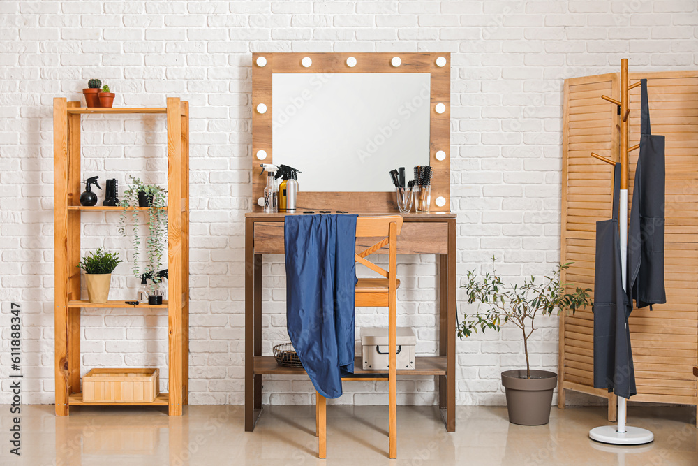 Different hairdressing tools on table near light brick wall in salon