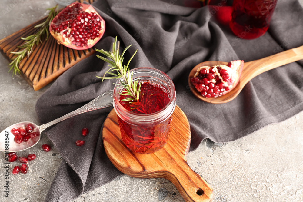 Spoon with fresh pomegranate and glasses of juice on grey table