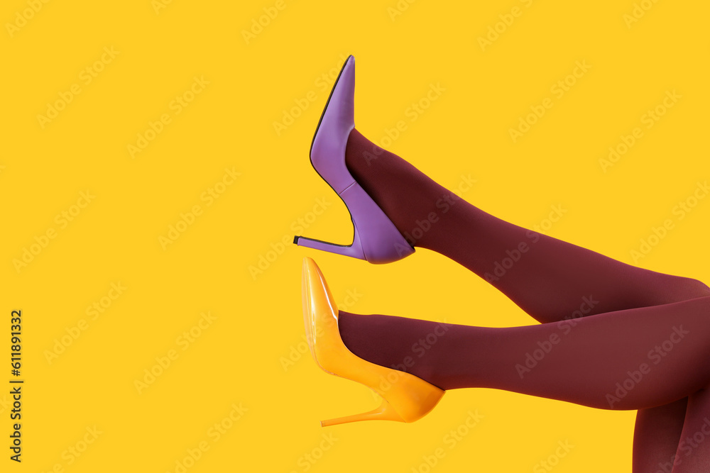 Female legs in black tights and different heels on yellow background