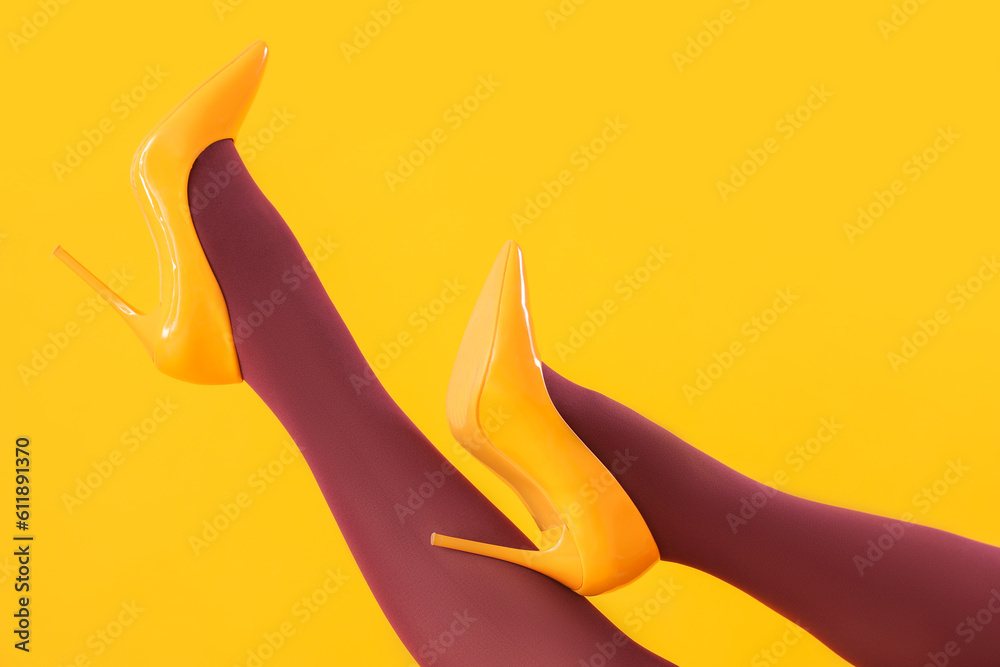 Female legs in black tights and high heels on yellow background