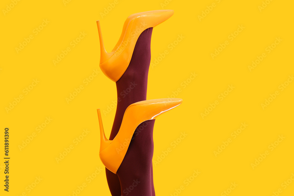 Female legs in black tights and high heels on yellow background