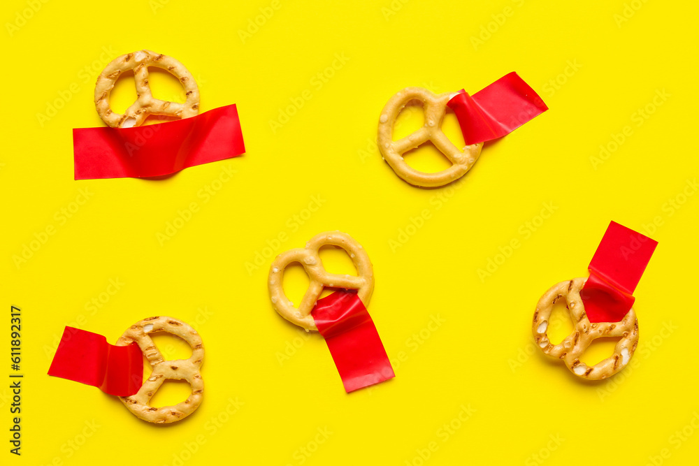 Tasty pretzels with adhesive tapes on yellow background