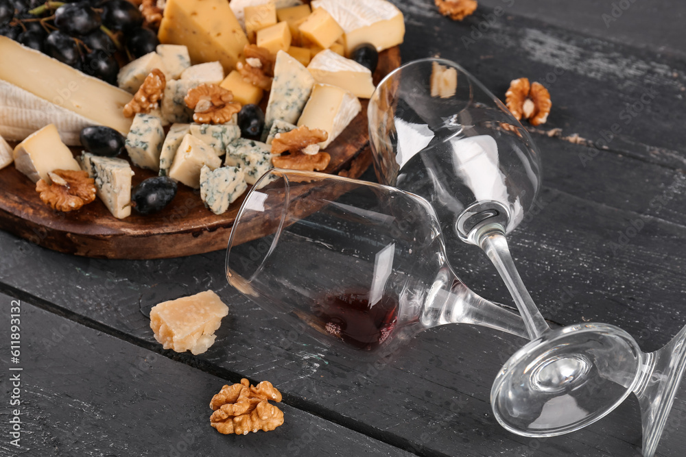 Plate with pieces of tasty cheese and wine glasses on dark wooden background